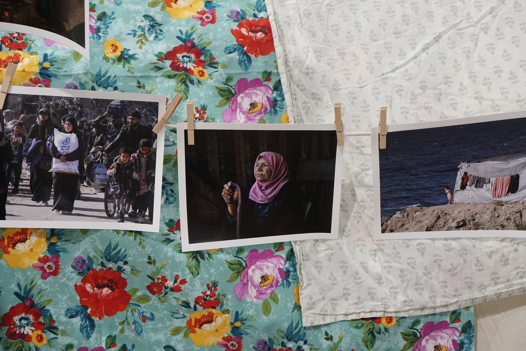 Varias fotografías dispuestas sobre fondos de tela con motivos florales. Las fotos muestran diversas escenas, entre ellas grupos de personas caminando, una mujer con un hiyab rosa y paisajes costeros con ropa tendida. Las telas presentan motivos florales de colores vivos en tonos turquesa, blanco y azul marino.